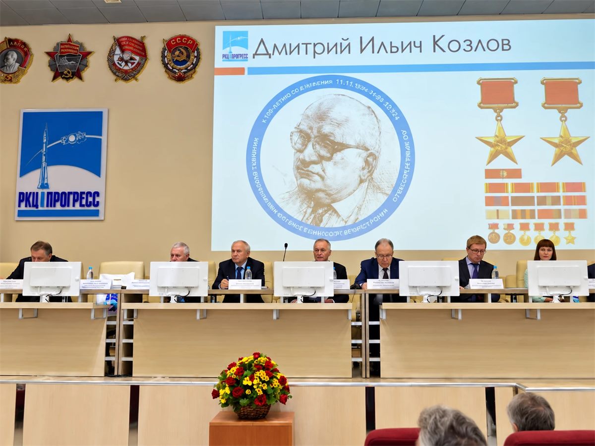 Президиум конференции в зале АО «РКЦ «Прогресс»; на экране — портрет Дмитрия Ильича Козлова